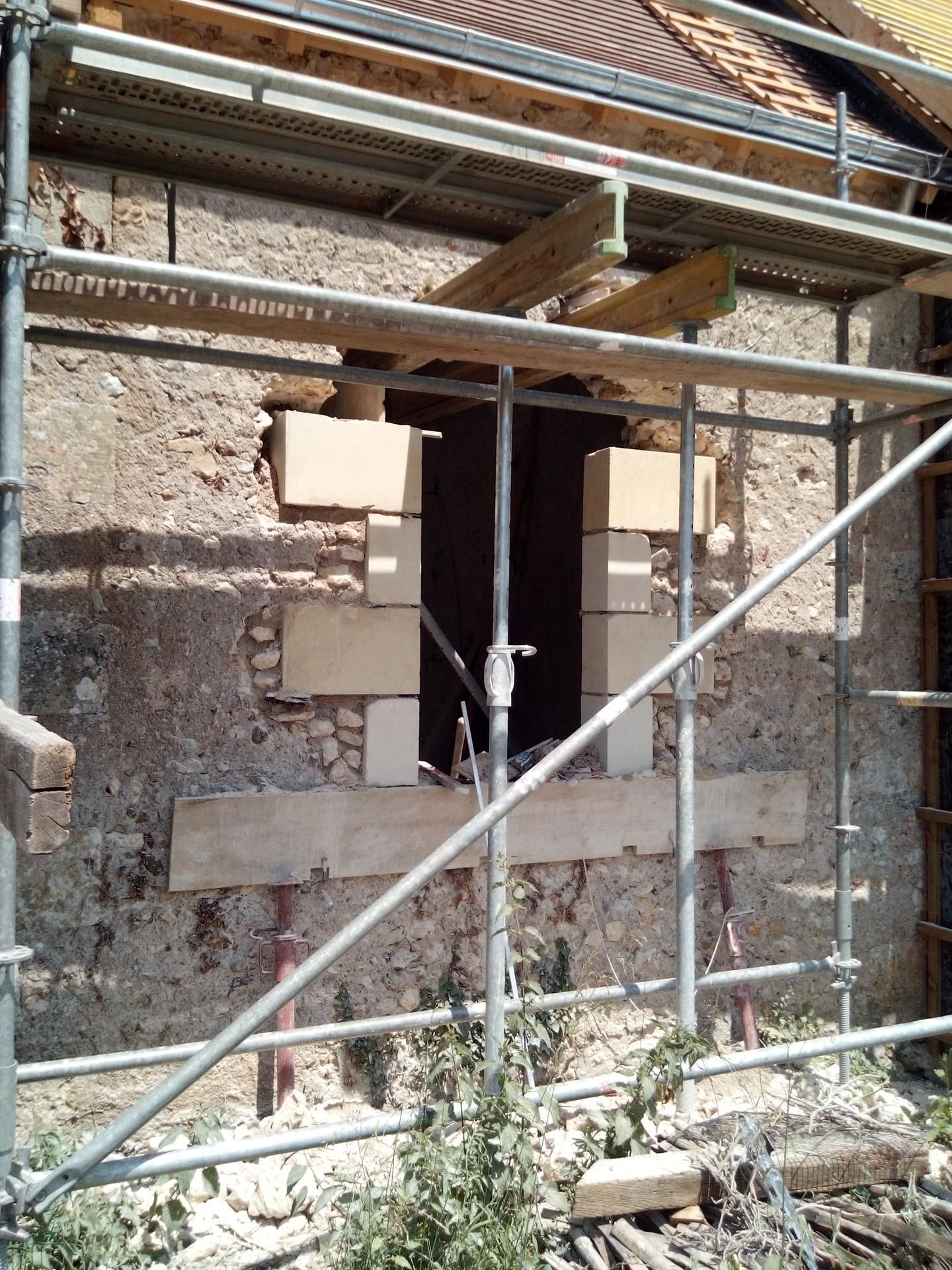 Rénovation du bâtiment : ouverture de fenêtre soutenue par un échafaudage et des poutres en bois, blocs de pierre utilisés pour la structure.