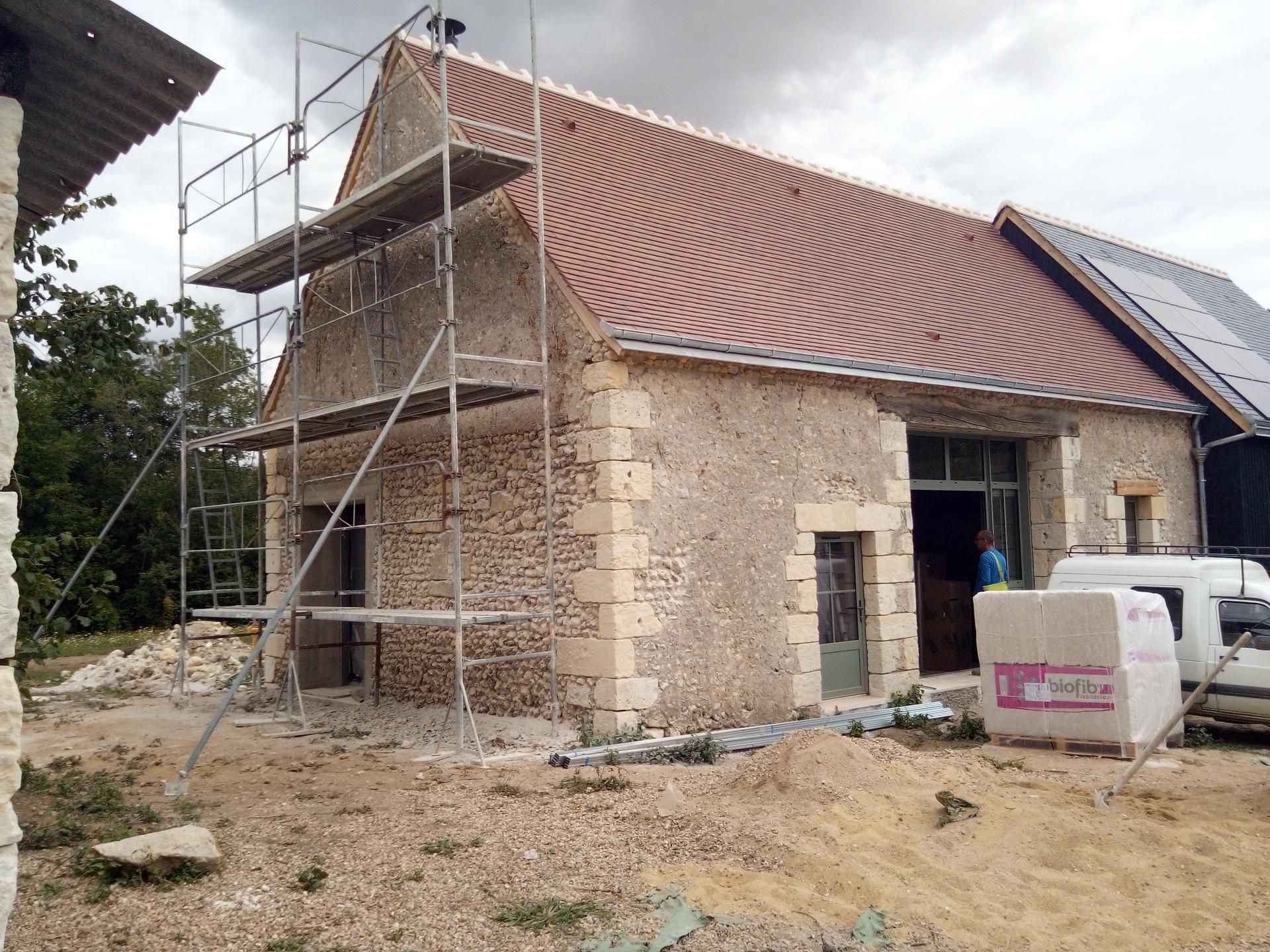 Bâtiment en pierre en cours de rénovation, avec échafaudages et toit de tuiles rouges.