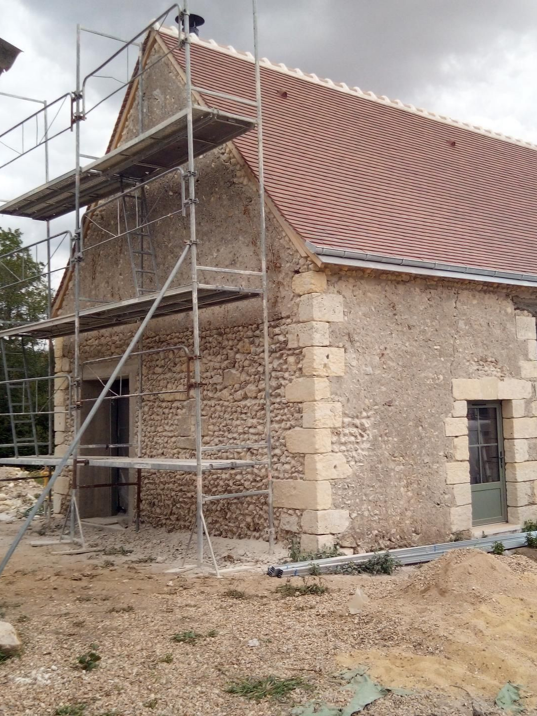 Bâtiment en pierre avec échafaudages, toit de tuiles en terre cuite et cour gravillonnée.