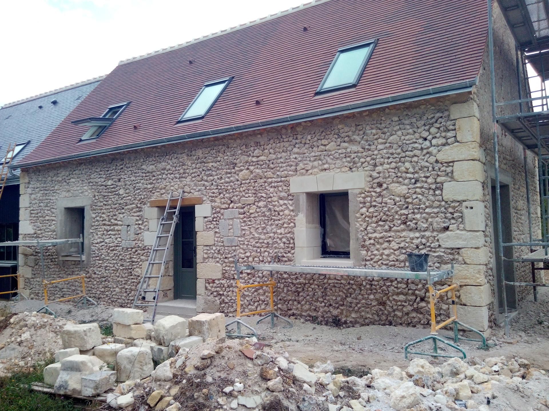 Bâtiment en pierre en cours de rénovation, avec toit de tuiles rouges, lucarnes et échafaudages.