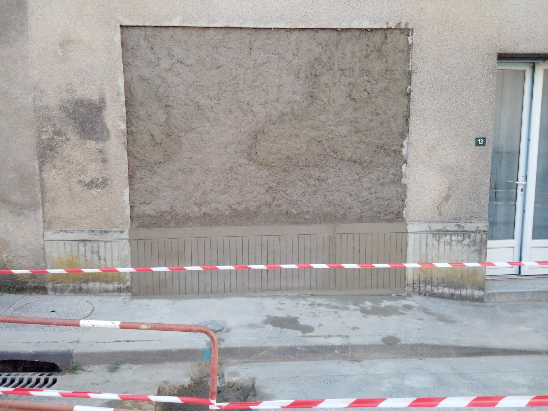 Mur extérieur avec fenêtre condamnée, réparation par enduit, ruban de signalisation rouge et blanc.