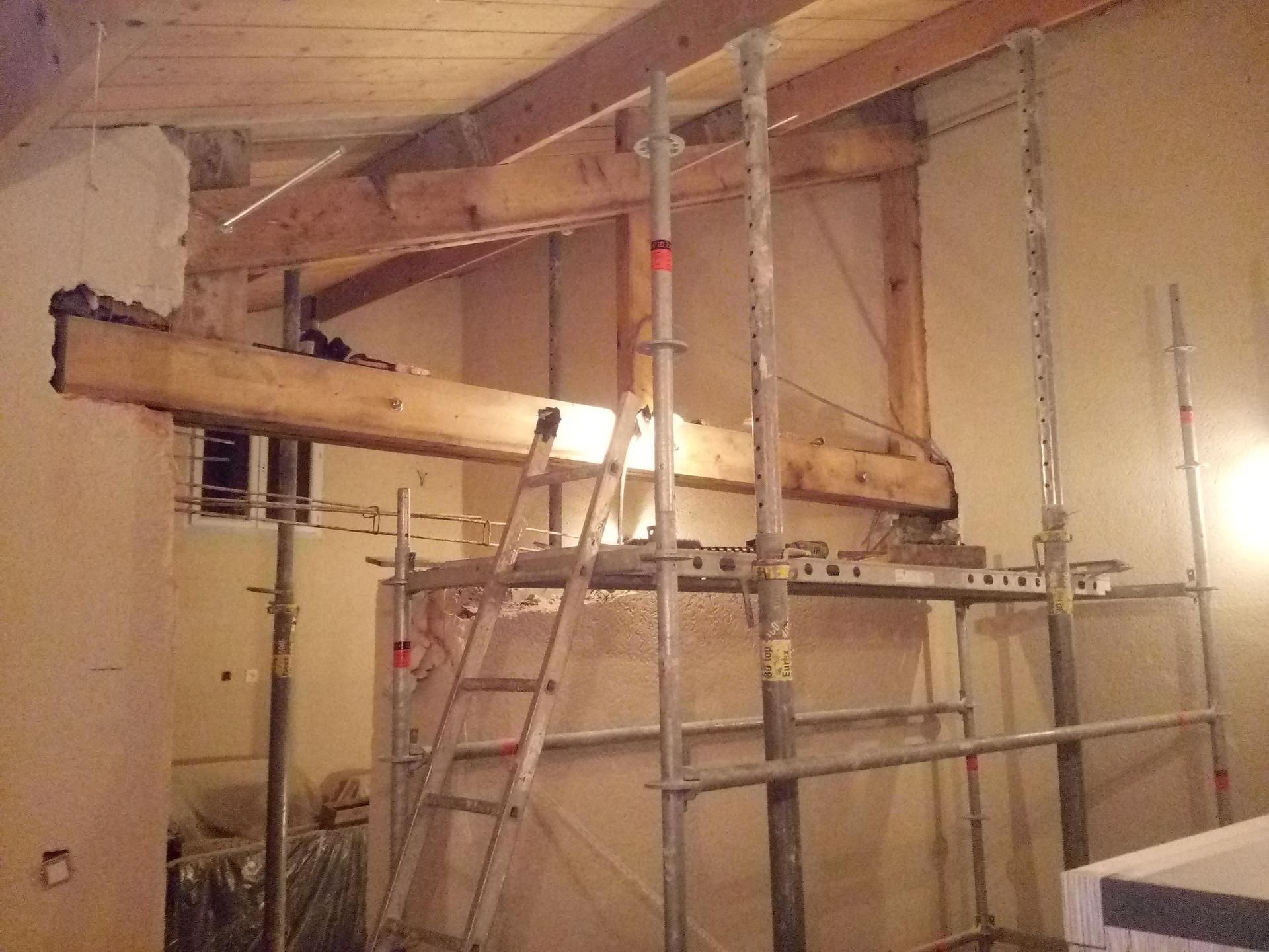 Vue intérieure d'un chantier de construction : poutres en bois, échafaudages et échelle à l'intérieur d'une pièce.