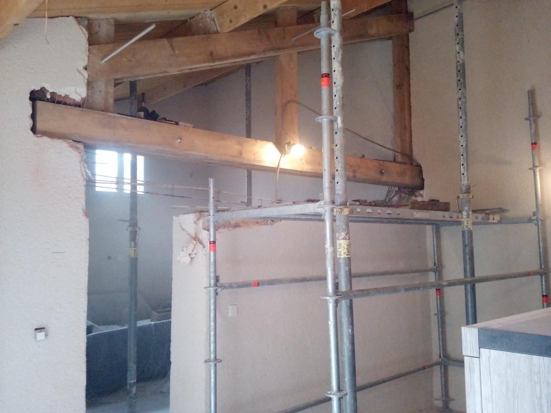 Intérieur avec poutres en bois apparentes, échafaudages de chantier et murs partiellement construits.