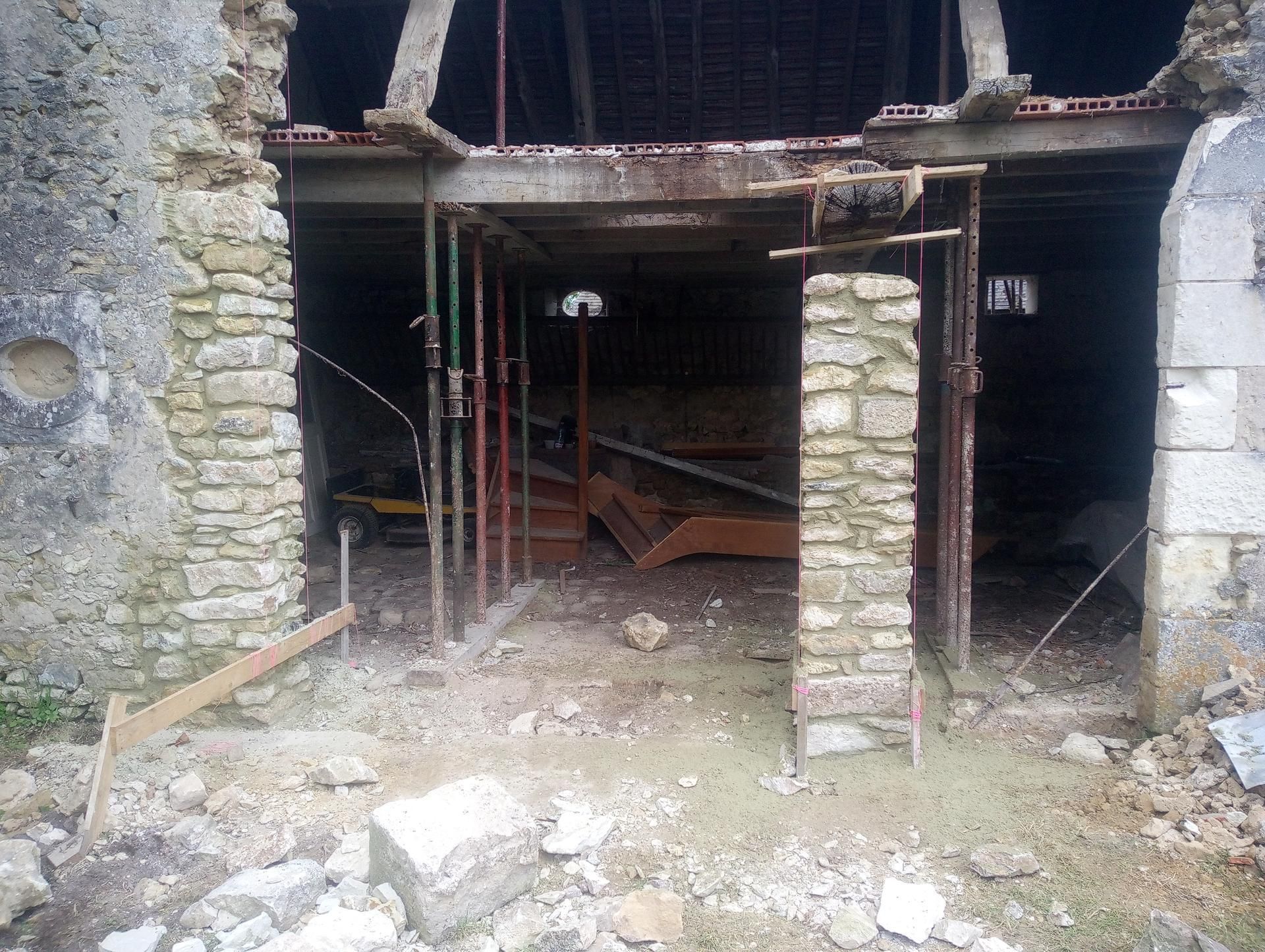 Vue extérieure d'un bâtiment en construction. Les poutres de soutien et les échafaudages sont en place ; porte ouverte.