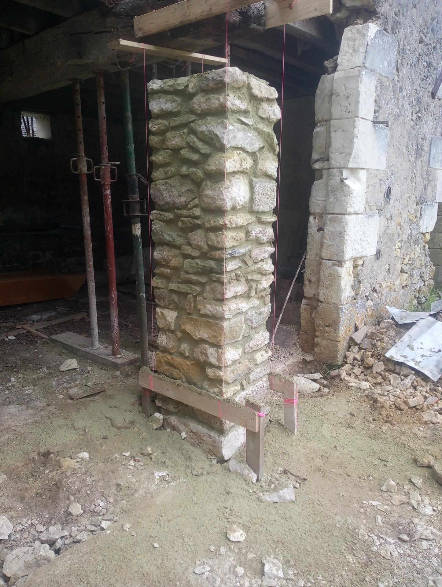 Colonne en pierre en construction, soutenue par un échafaudage en métal et en bois ; décor intérieur.