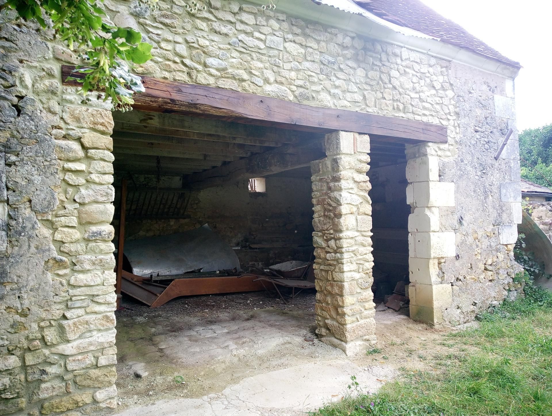 Extérieur d'un bâtiment en pierre patinée par le temps, avec une porte ouverte ; intérieur en métal rouillé.