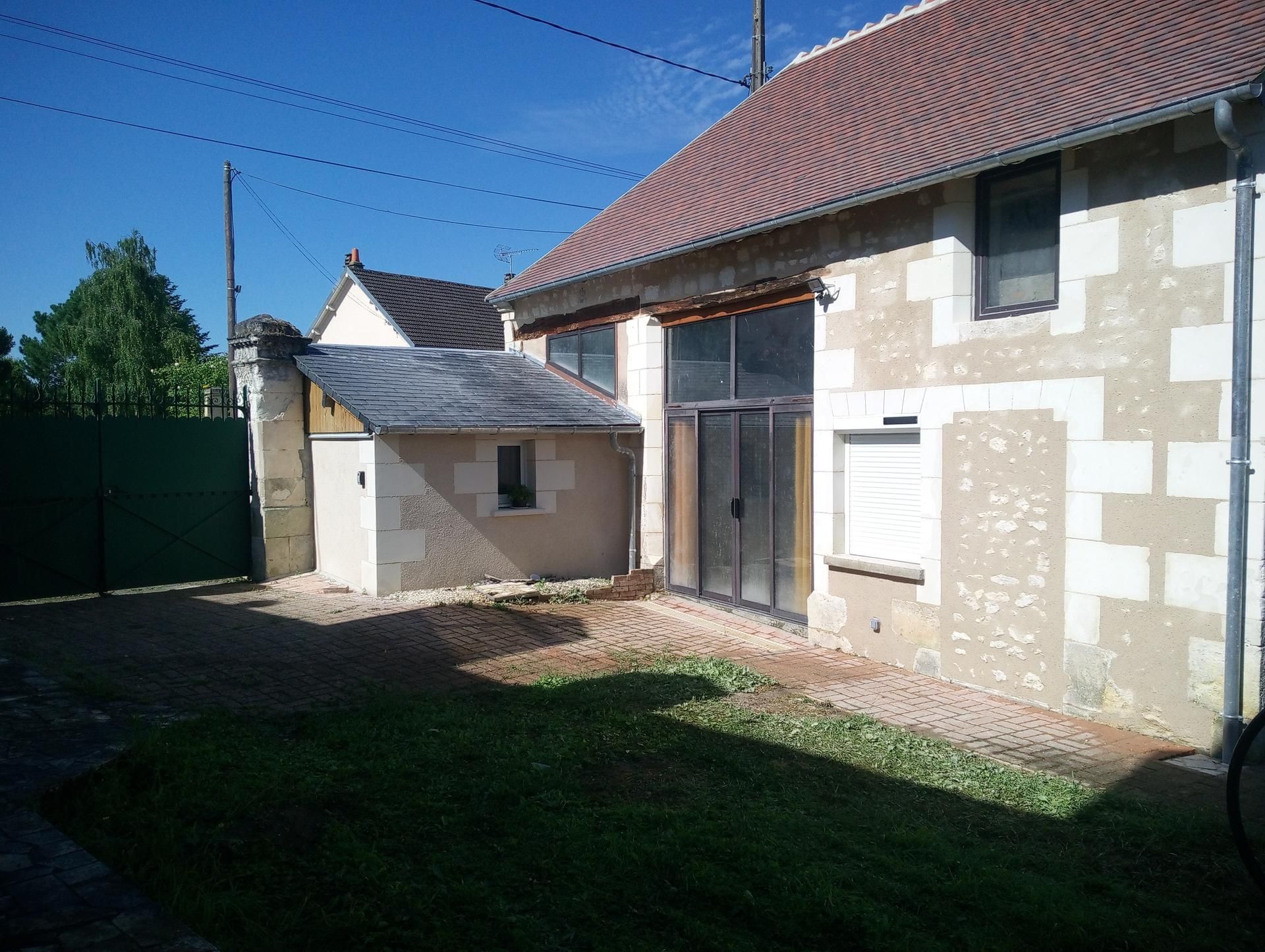 Bâtiment en pierre avec un petit abri et une pelouse. Toit de tuiles brunes.