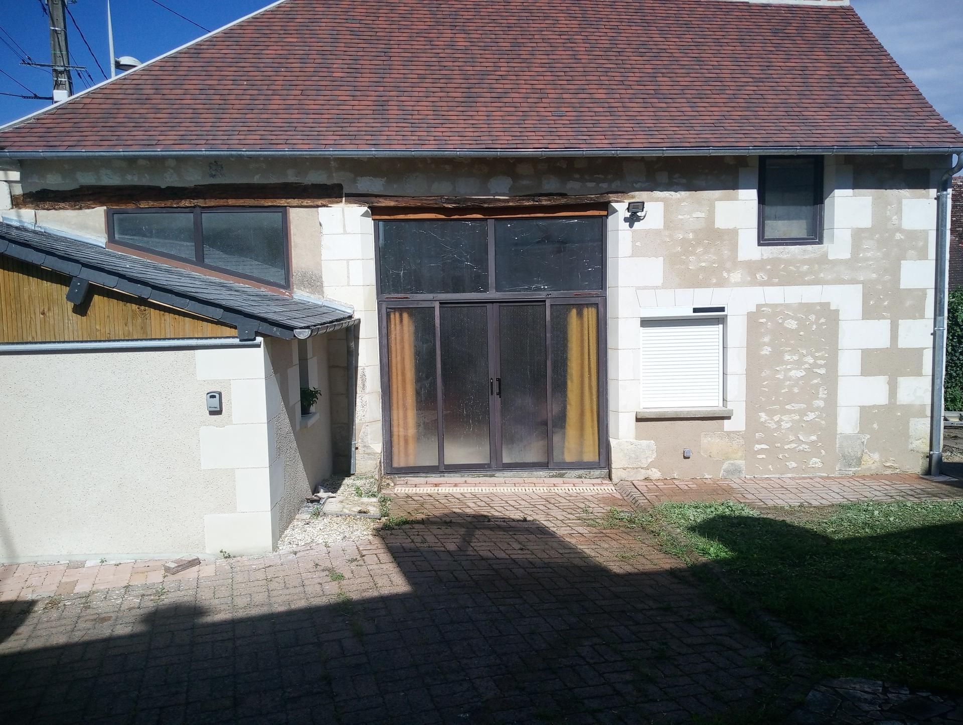 Bâtiment en pierre avec portes coulissantes en verre, toit brun et petites fenêtres ; allée pavée devant.