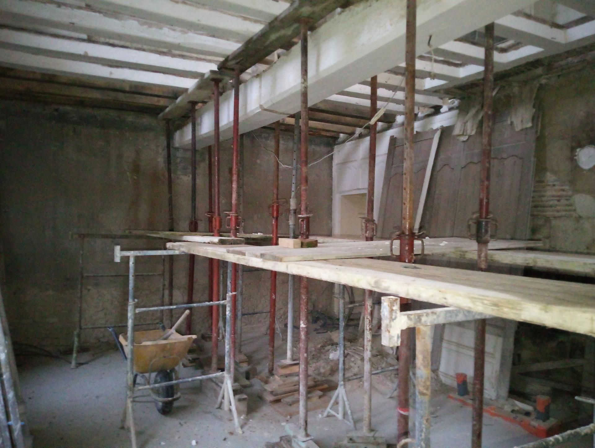 Vue intérieure d'un chantier de construction avec des structures de soutien temporaires sous un plafond.