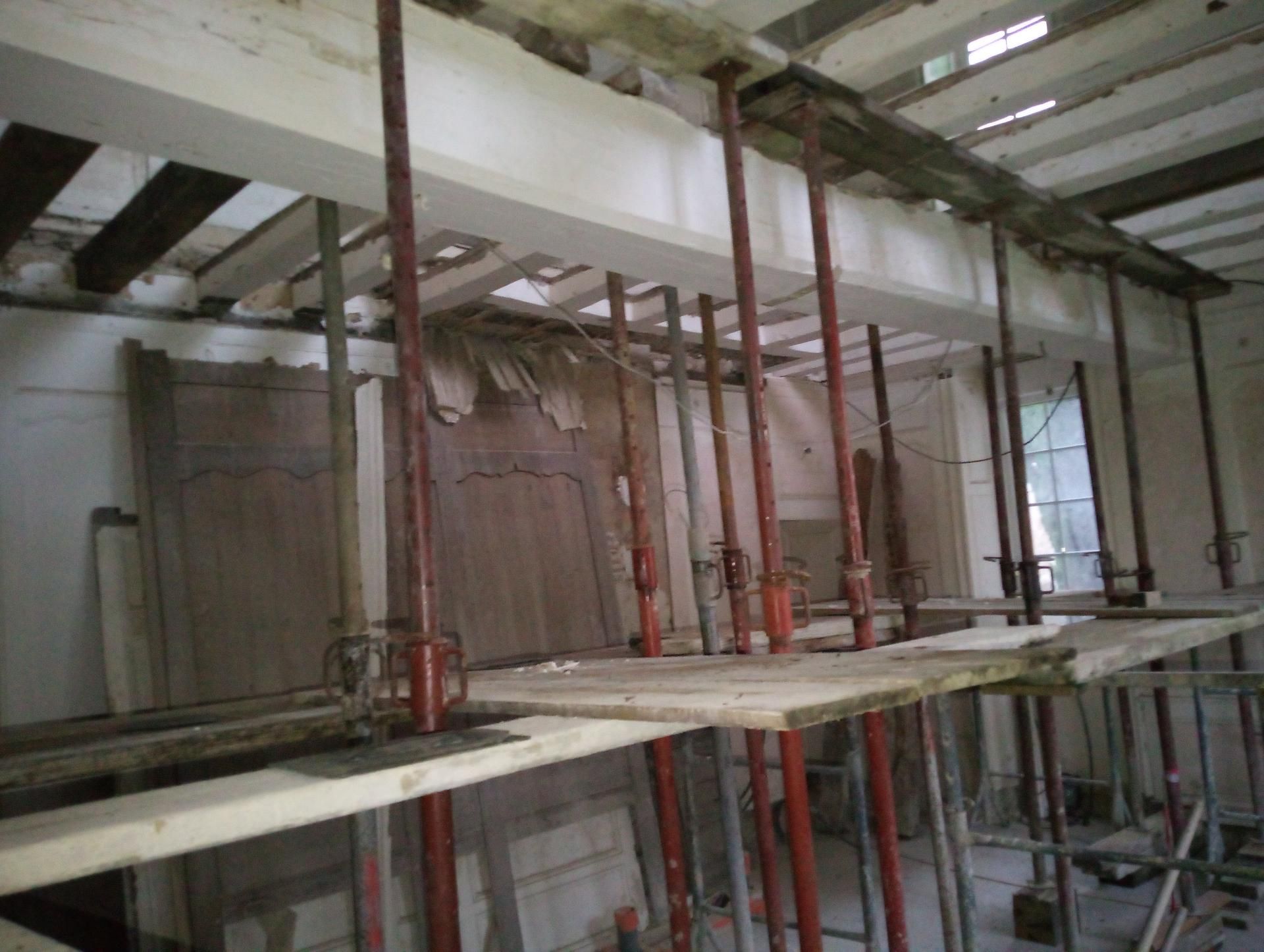 Vue intérieure d'un bâtiment en construction, montrant des échafaudages et des poutres de soutien.