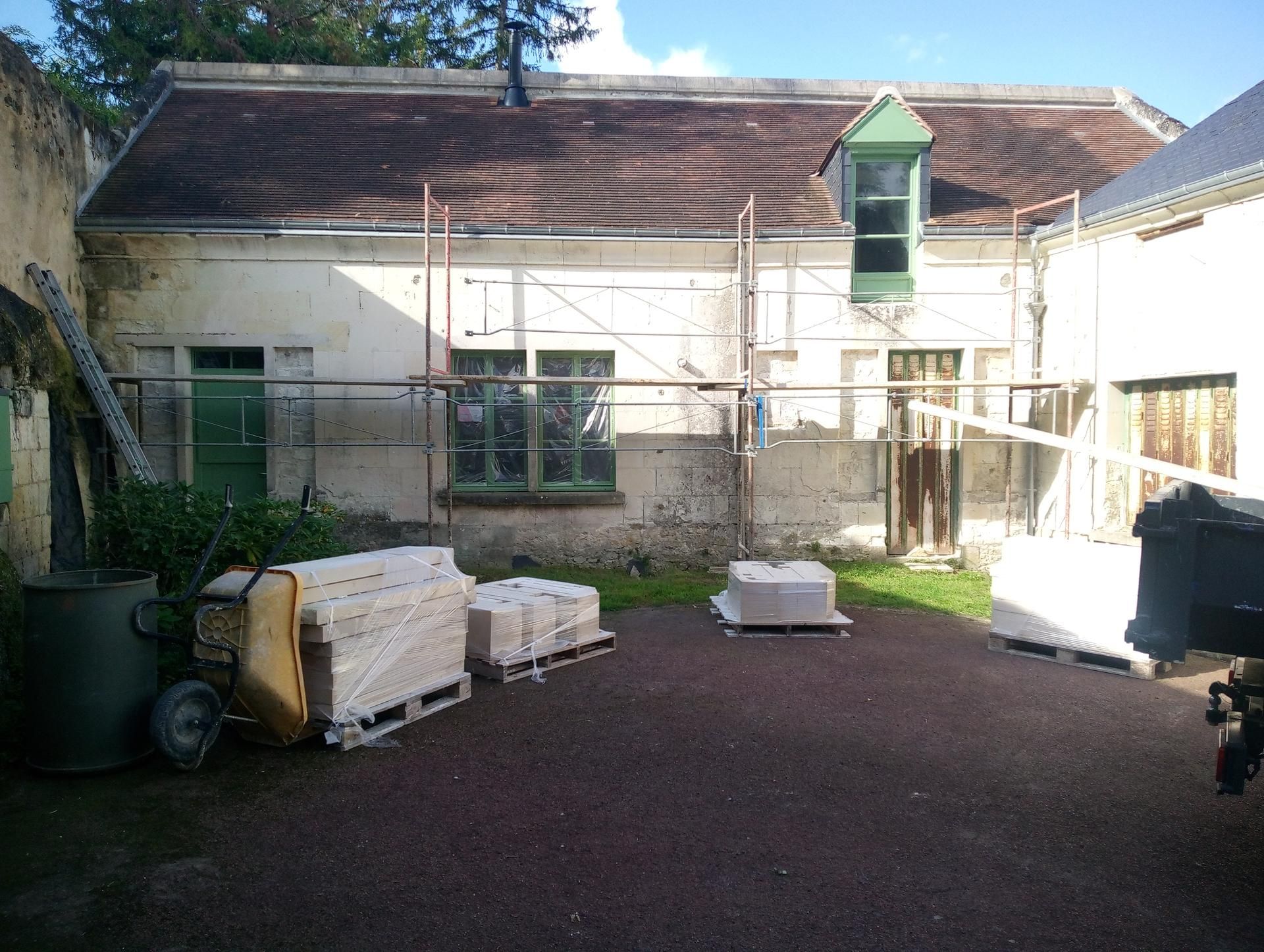 Bâtiment en rénovation avec échafaudages, palettes de matériaux et une porte verte.
