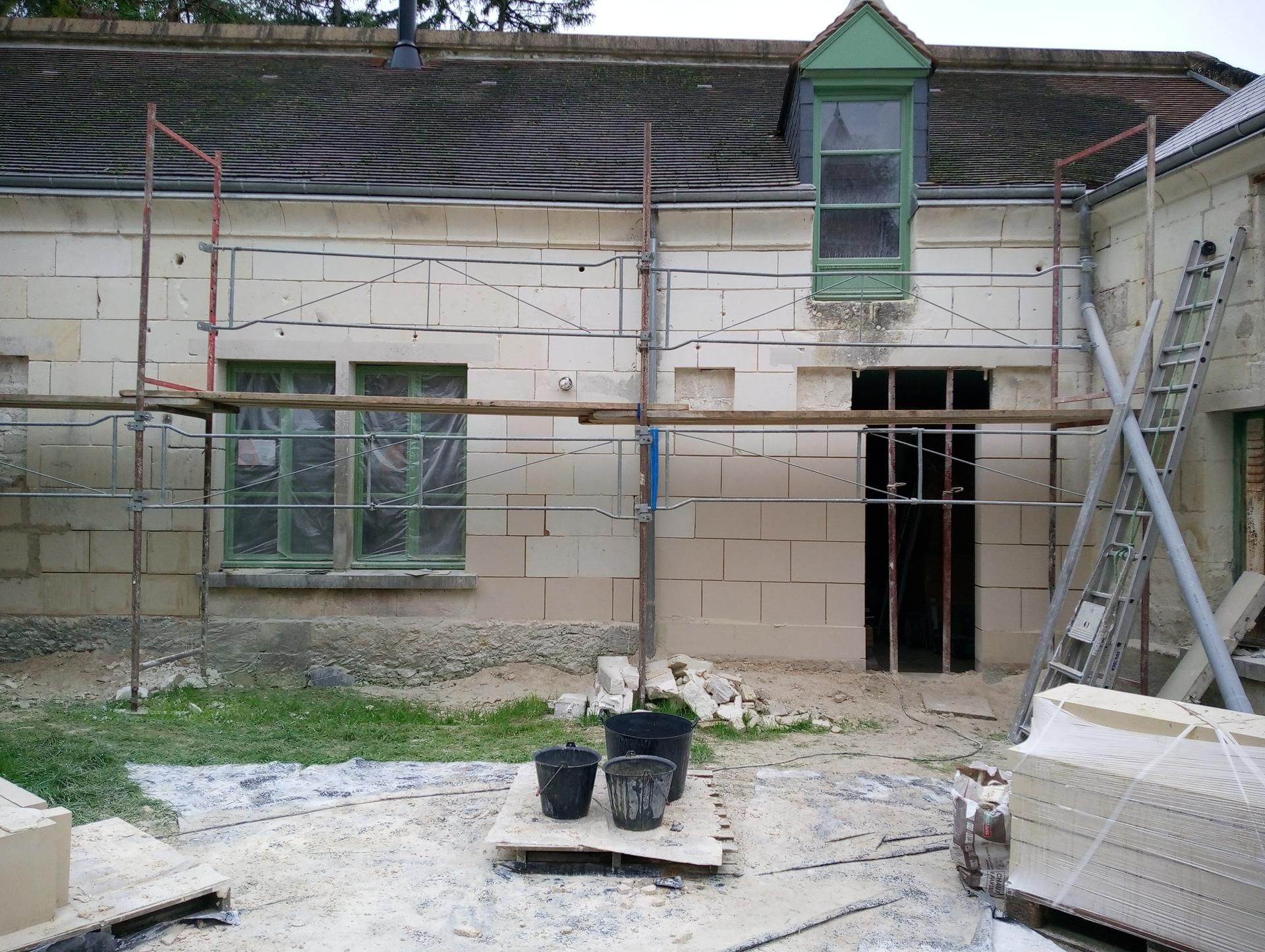Mur extérieur d'un bâtiment en construction, avec fenêtres, échafaudages et blocs de couleur claire.