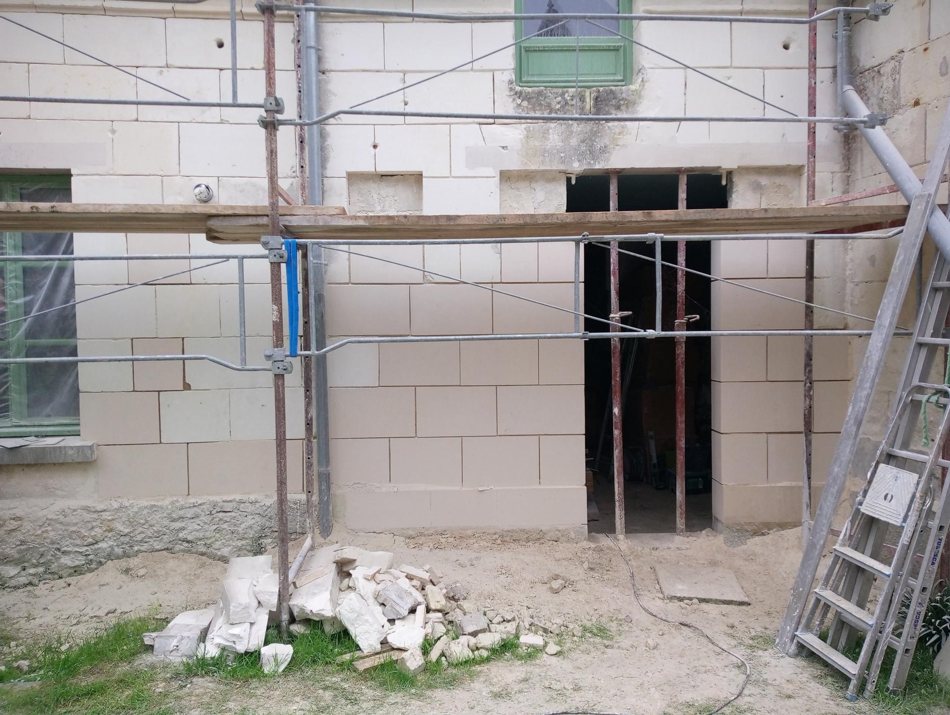 Extérieur du bâtiment en construction avec échafaudages et une ouverture de porte.