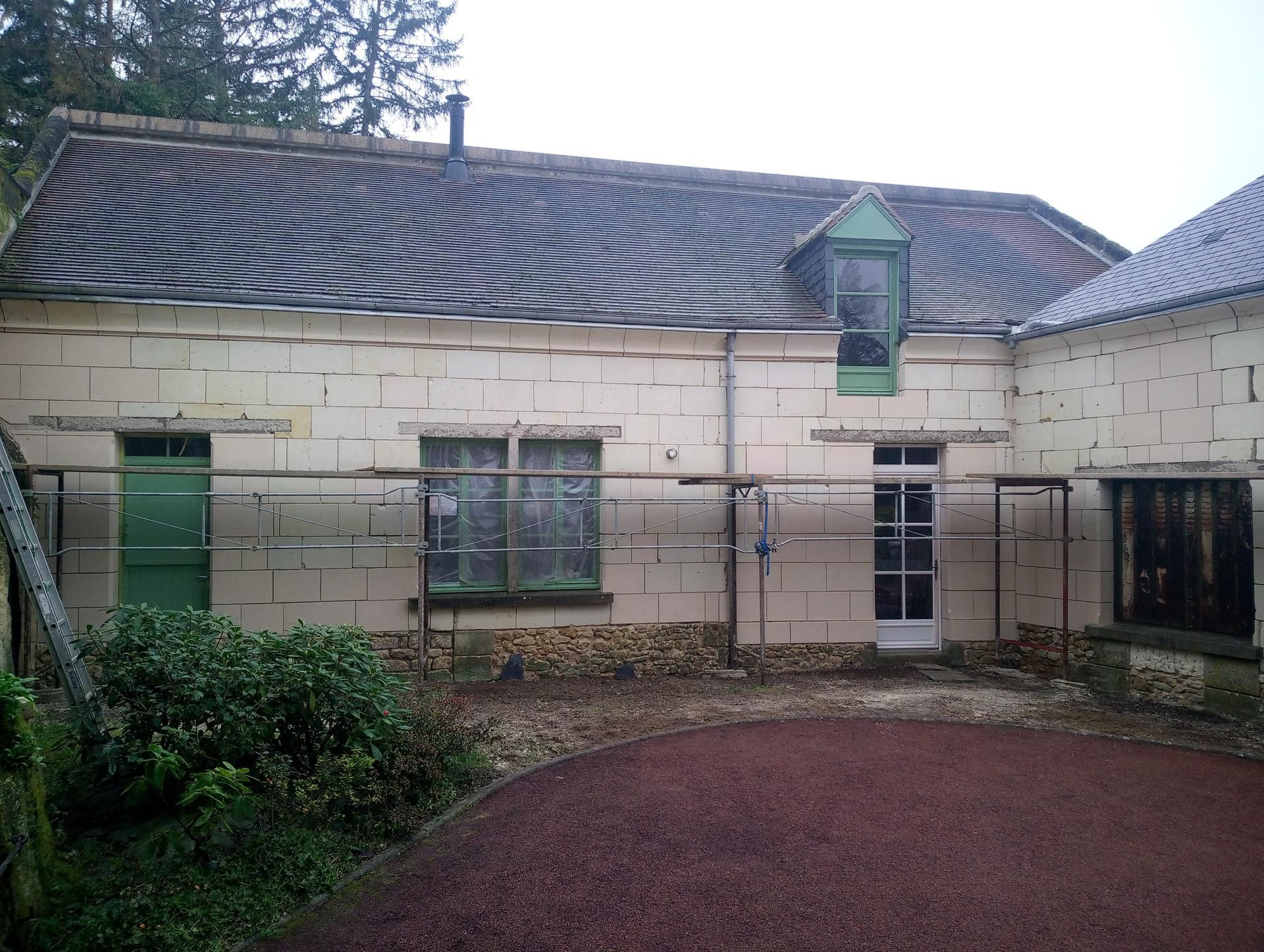 Bâtiment au toit ondulé, plusieurs fenêtres et une porte verte. Le sol est recouvert de gravier rouge.