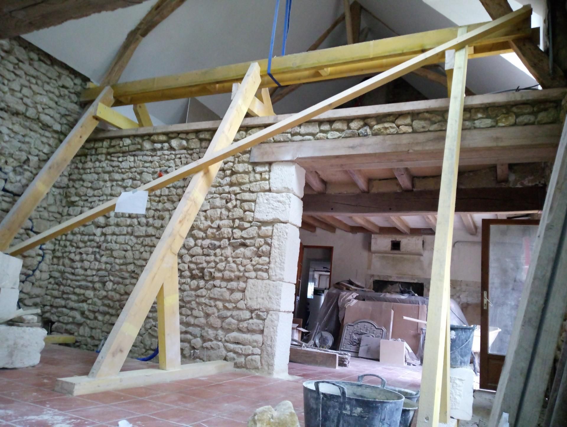 Travaux intérieurs : Des étais en bois temporaires soutiennent un mur et un plafond en pierre ; l'embrasure de la porte est visible.