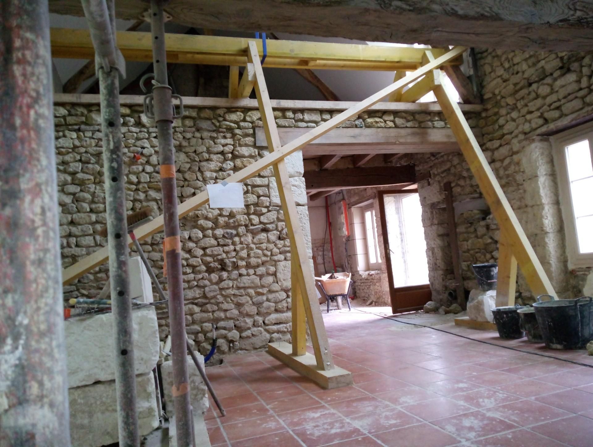 Rénovation intérieure avec charpente en bois soutenant un plafond au-dessus d'une porte. Murs en pierre et sol en terre cuite.