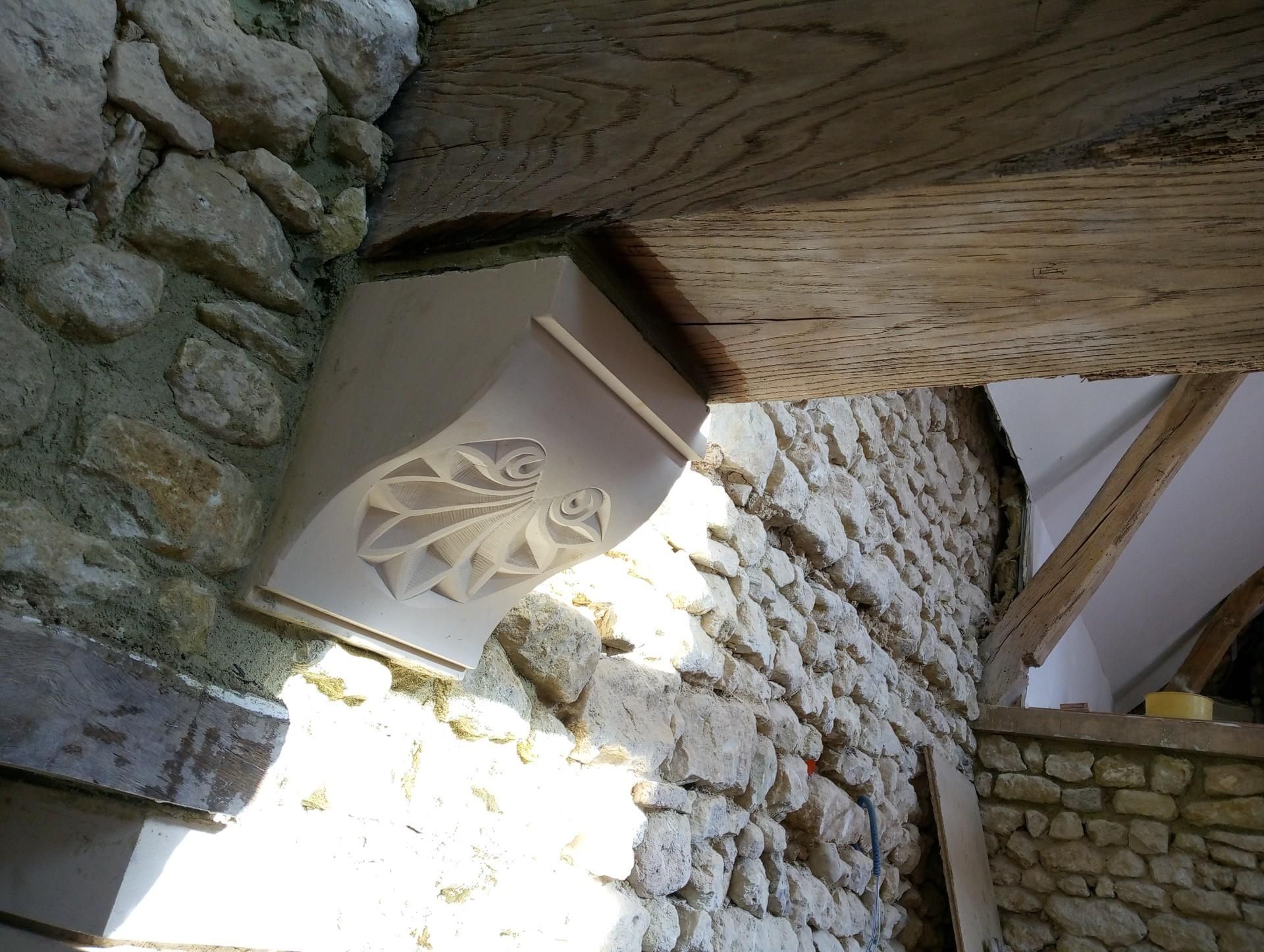 Mur en pierre orné de détails décoratifs sculptés soutenant une poutre en bois.
