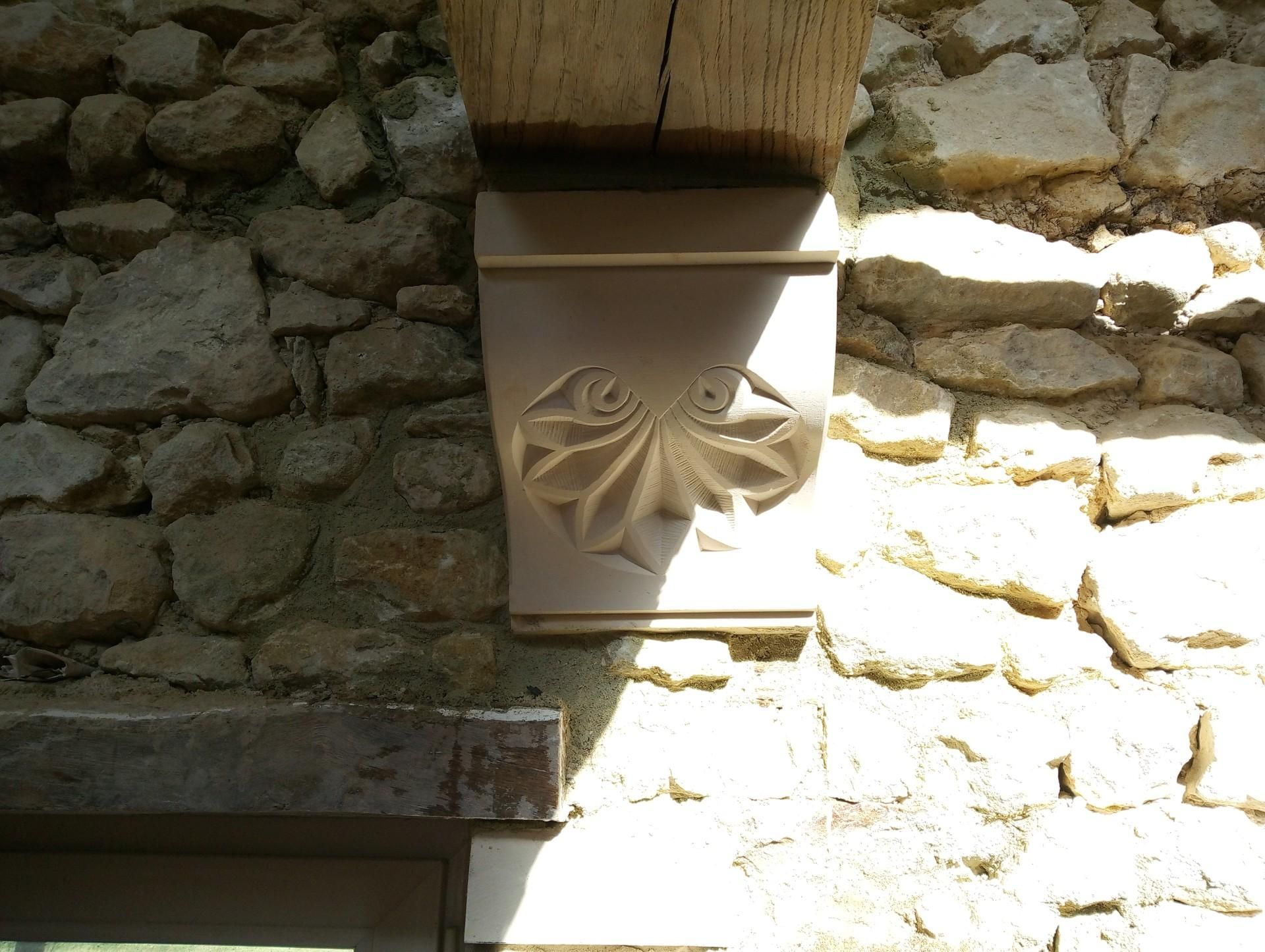 Console en pierre ornée de motifs floraux sculptés soutenant une poutre en bois, encastrée dans un mur en pierre.