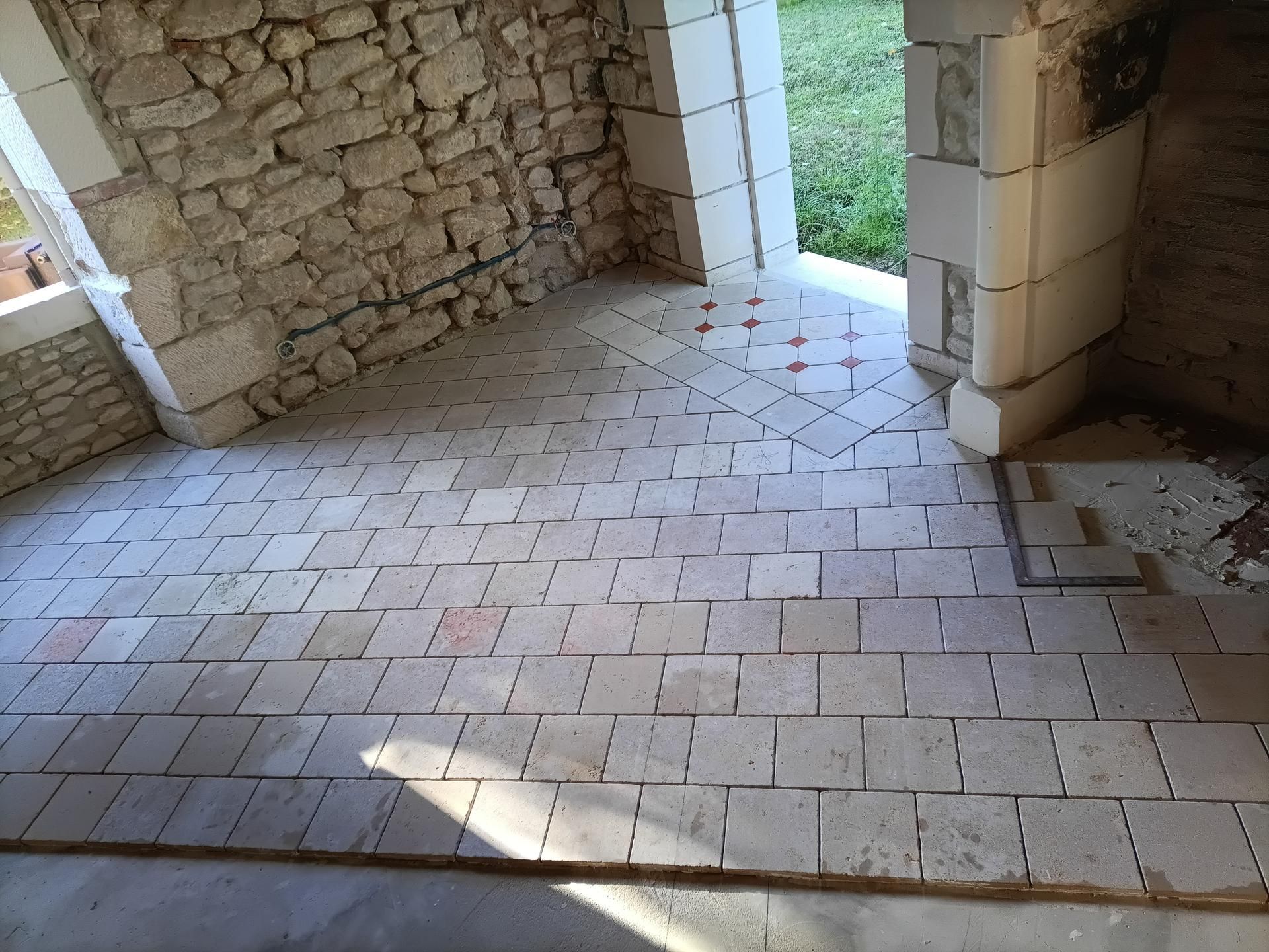 Sol carrelé en pierre dans une pièce aux murs en pierre et avec une porte ouverte sur l'extérieur.