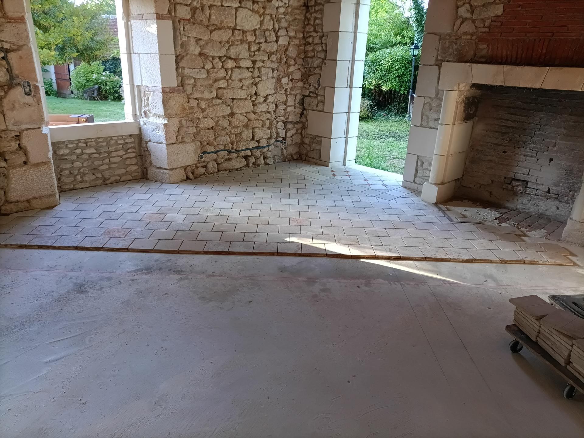 Vue intérieure d'un bâtiment en construction, montrant des murs en pierre, une porte ouverte et un sol partiellement fini.