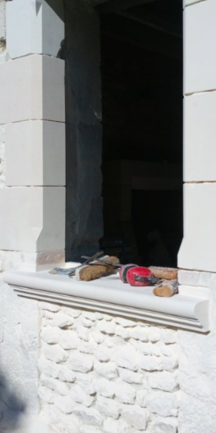 Ouverture de fenêtre avec appui en pierre, outils sur l'appui, mur en blocs de pierre en dessous.