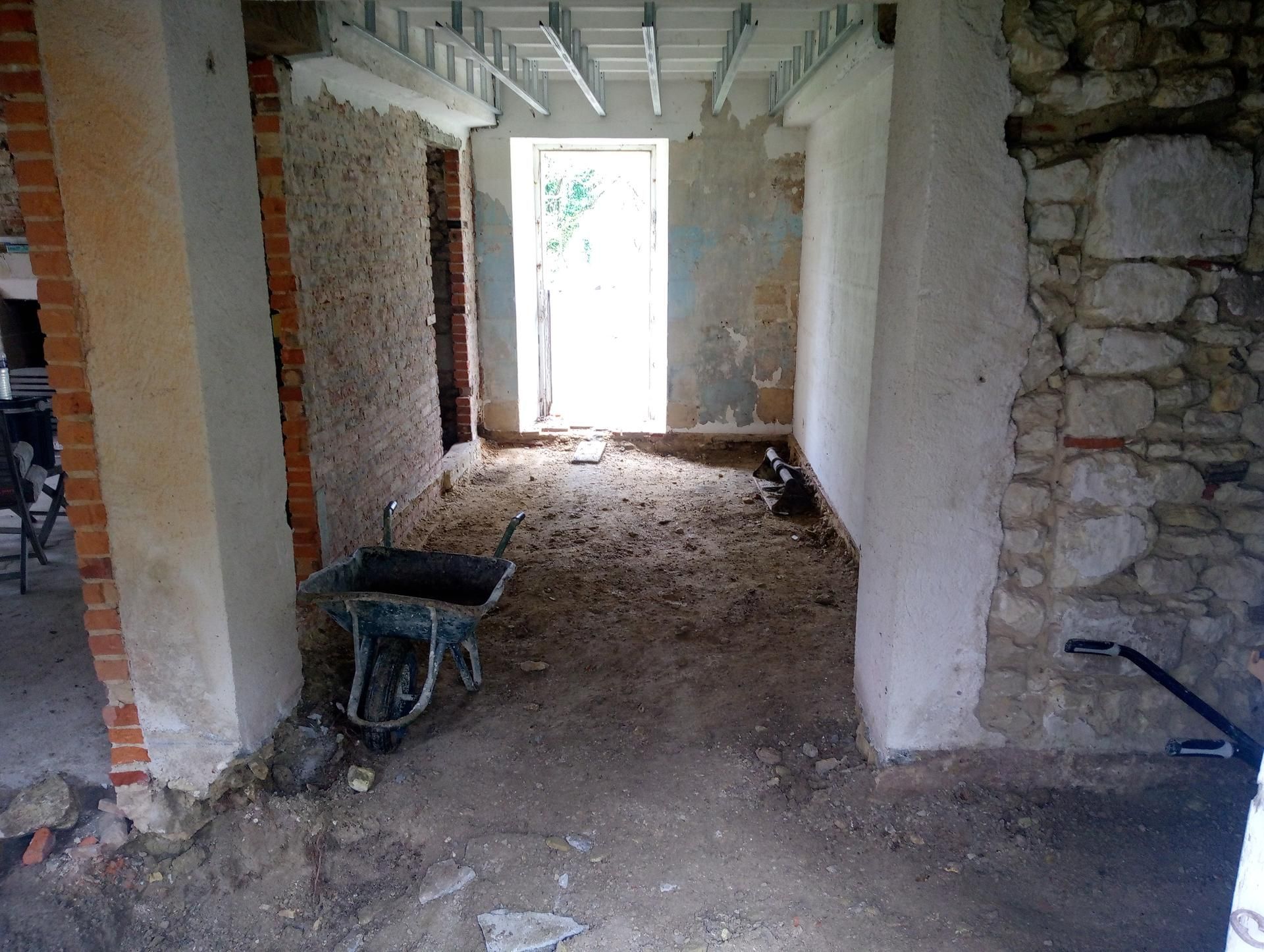 Rénovation en cours ; pièce avec briques apparentes, murs en pierre, porte ouverte et brouette.