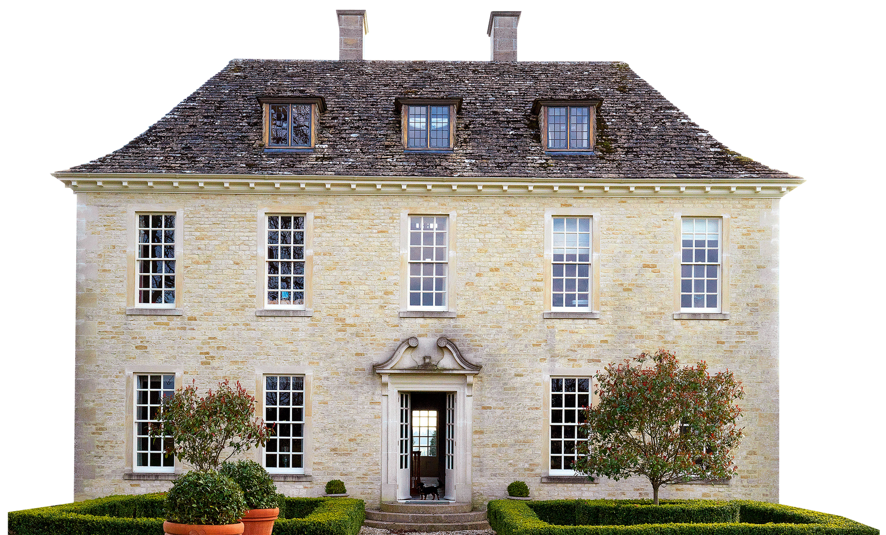 Maison en pierre de deux étages avec un toit en ardoise, des fenêtres symétriques et un jardin soigné.