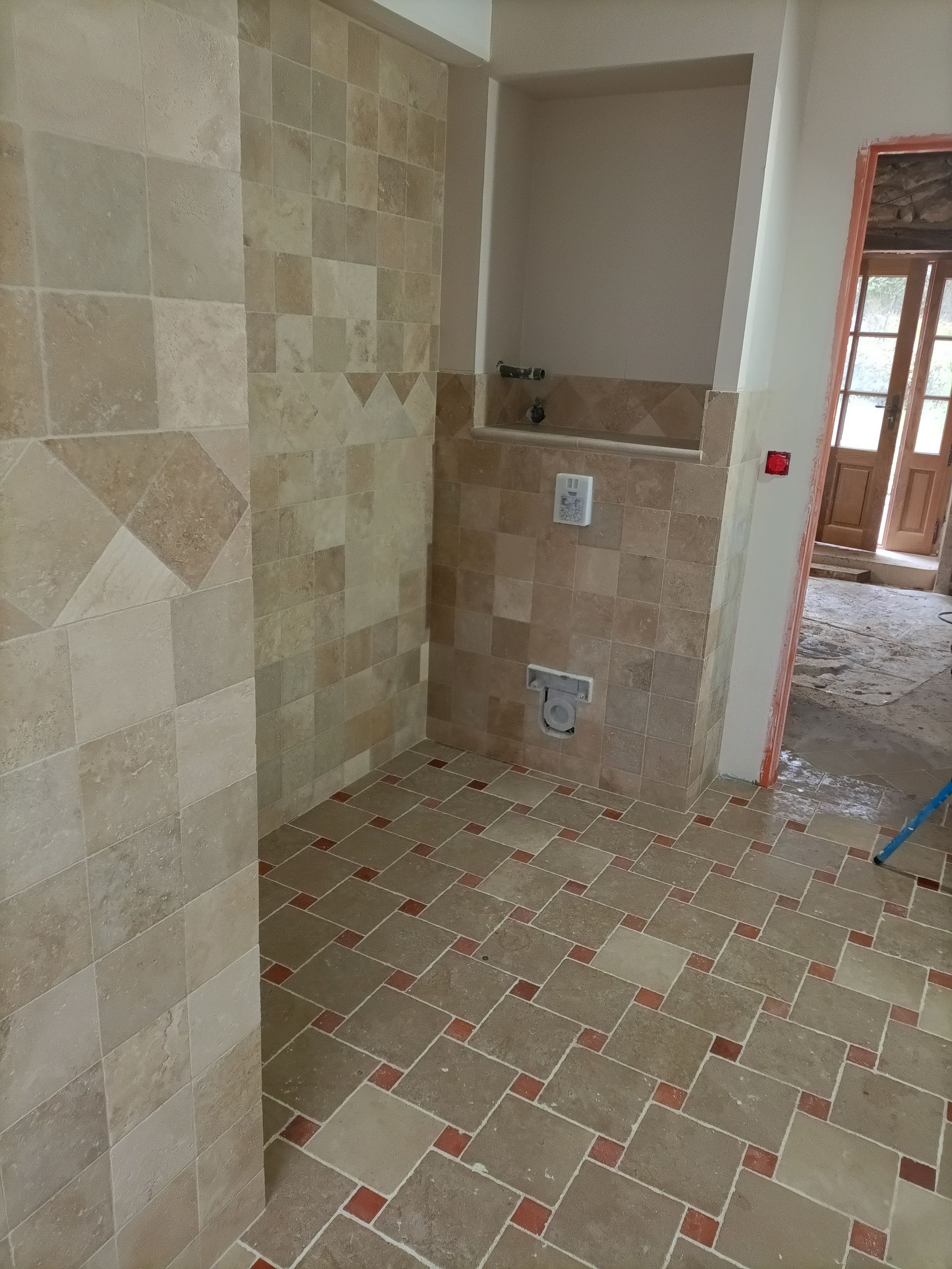 Salle de bains avec murs et sol carrelés, tons neutres et une alcôve pour les équipements sanitaires.