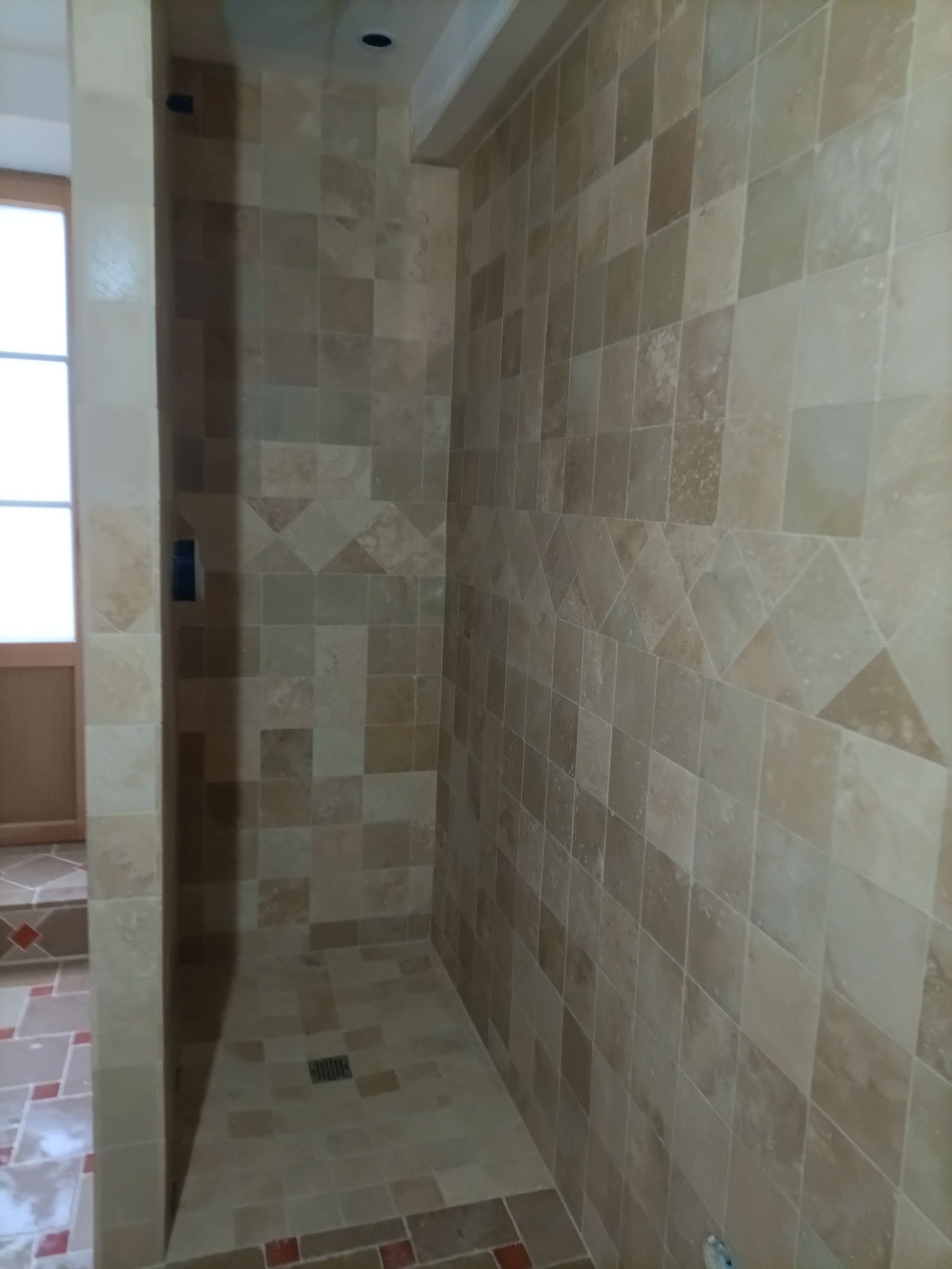 Cabine de douche carrelée avec des carreaux de pierre brun clair ; bonde visible.