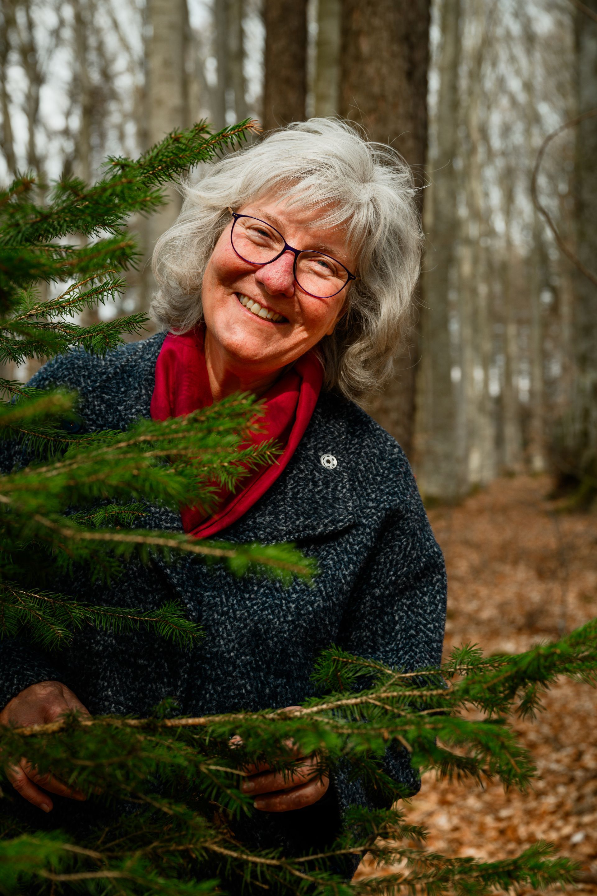Une femme sourit en tenant un sapin de Noël dans les bois.