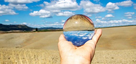 Une personne tient une boule de verre dans sa main devant un champ.