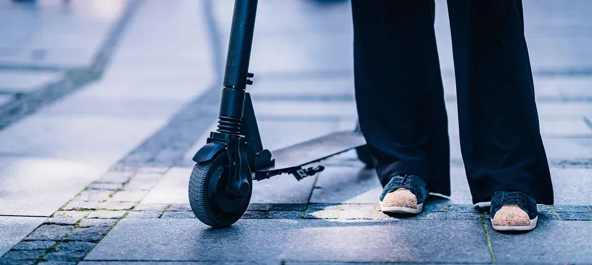 Una mujer está parada en una acera sosteniendo un scooter eléctrico.