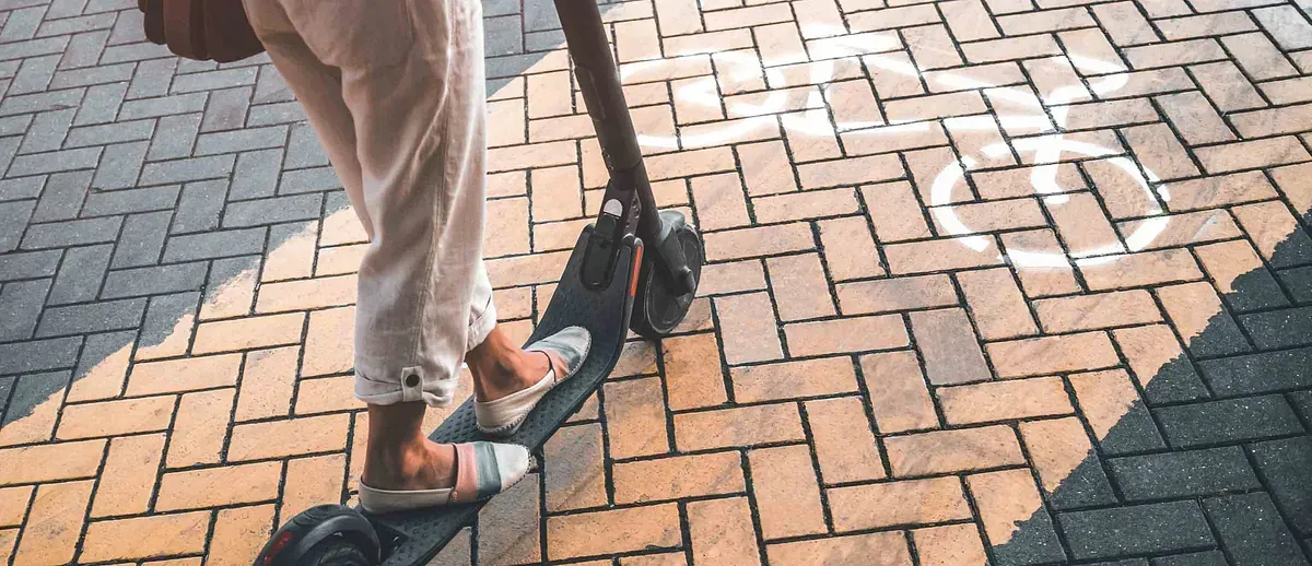 Una mujer va en patinete eléctrico por una acera de ladrillos.