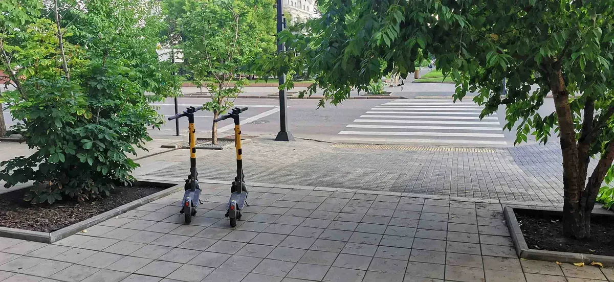 Dos scooters están estacionados en una acera al lado de un árbol.