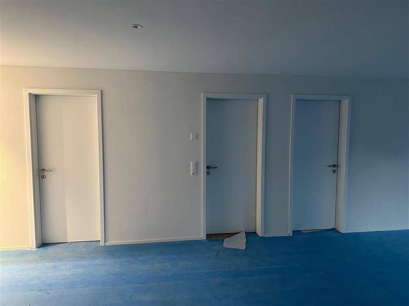 Drei weisse Türen an einer weissen Wand in einem Raum mit blauem Fussboden.