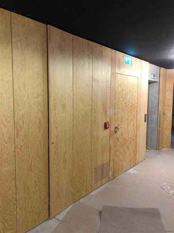 Holzvertäfelte Wand mit Tür, Feuermelder, Lüftungsöffnung und Aufzugszugang.