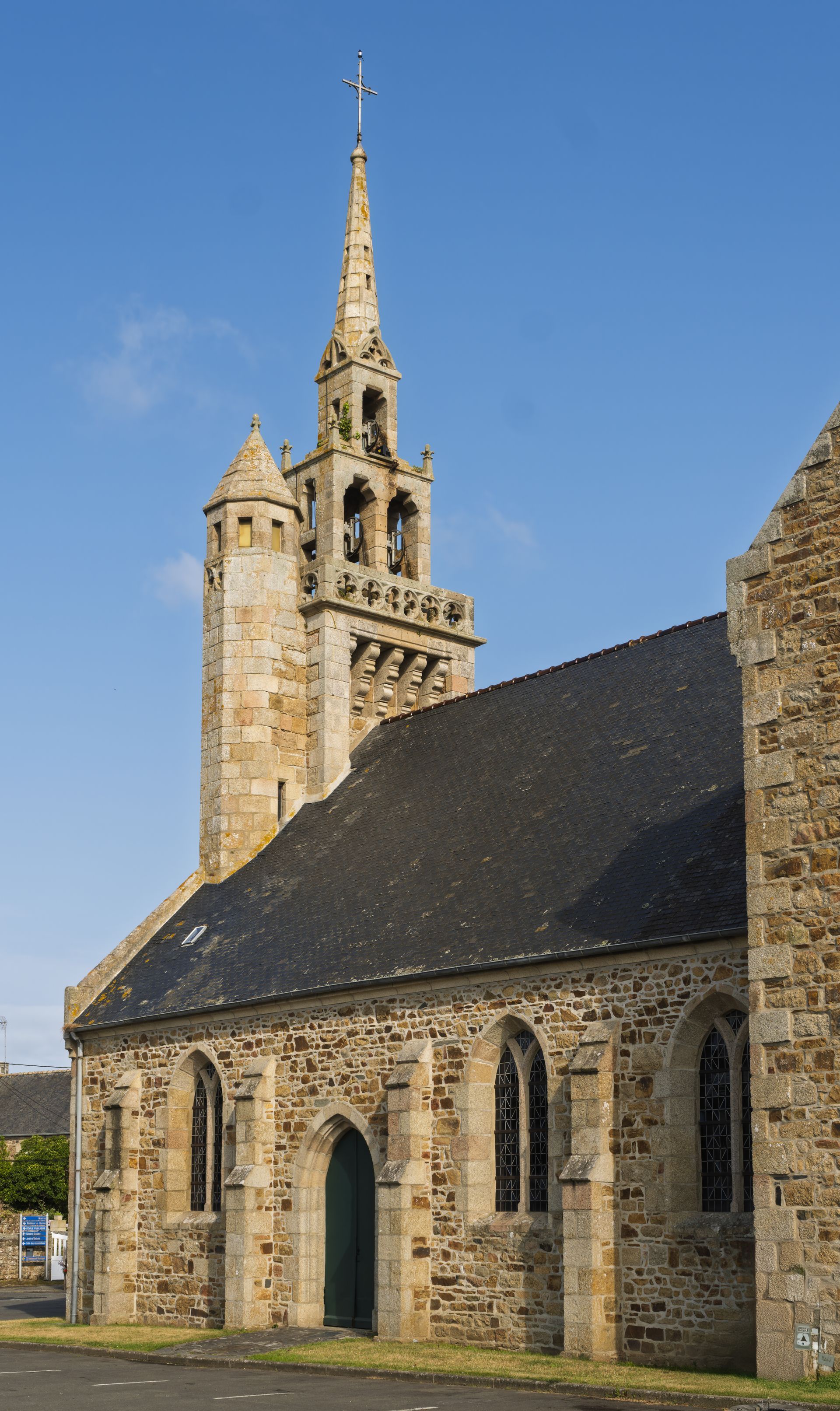 Église en pierre avec un haut clocher contre un ciel bleu.