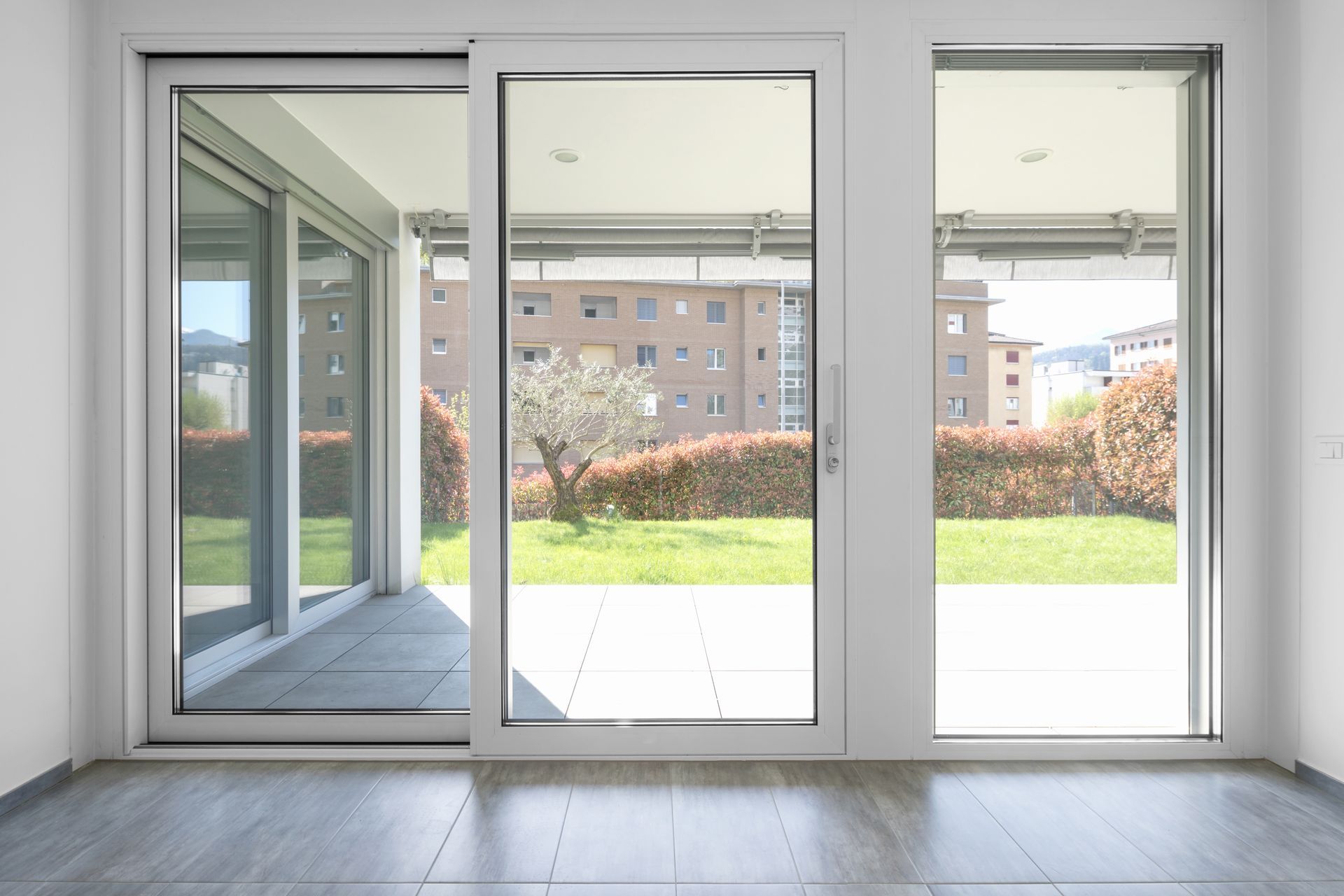 Porte-fenêtre coulissante en verre donnant sur une cour avec verdure et bâtiments.