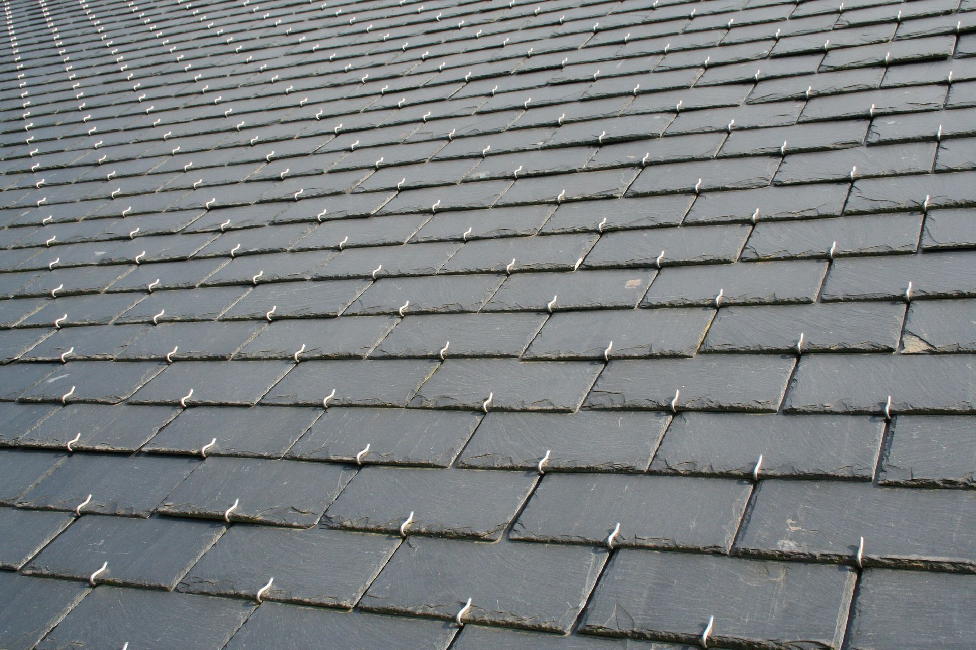 Vue rapprochée d'un toit en ardoise avec des tuiles gris foncé, montrant la texture et les détails de fixation.