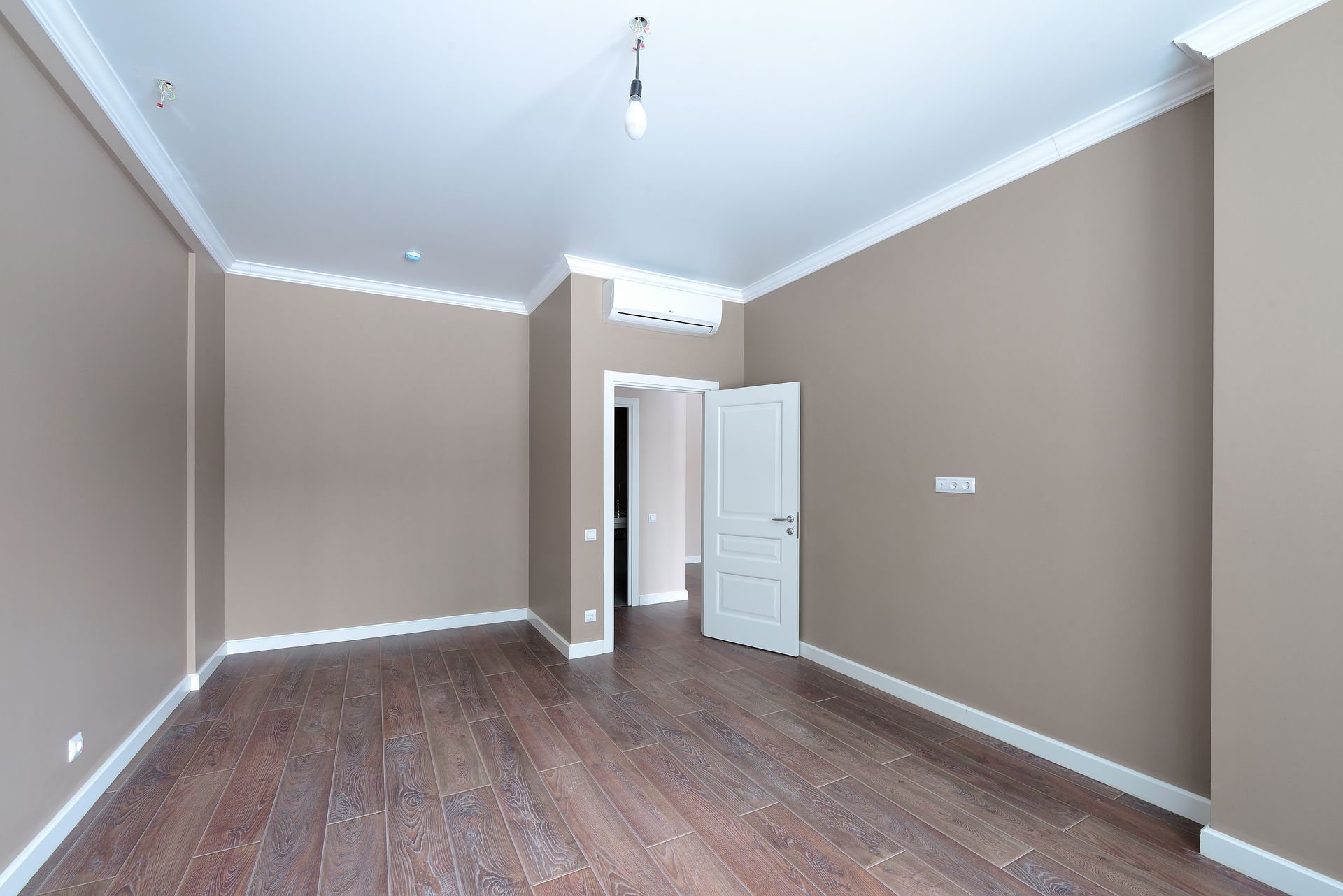 Pièce vide aux murs marron, aux boiseries blanches et au parquet foncé. Une porte ouvre sur une pièce plus sombre.