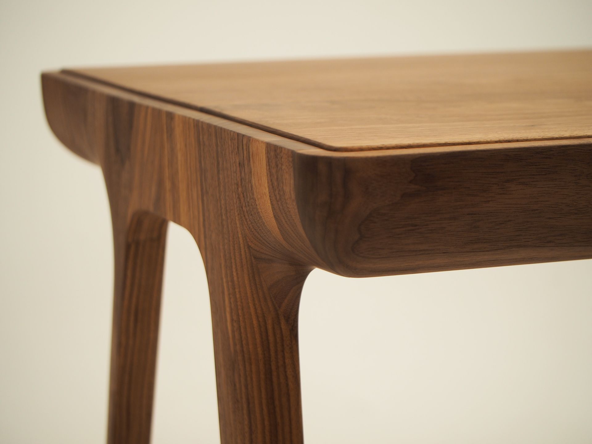 Gros plan d'un coin de table en bois ; pieds marron foncé et plateau marron clair, aux bords arrondis.