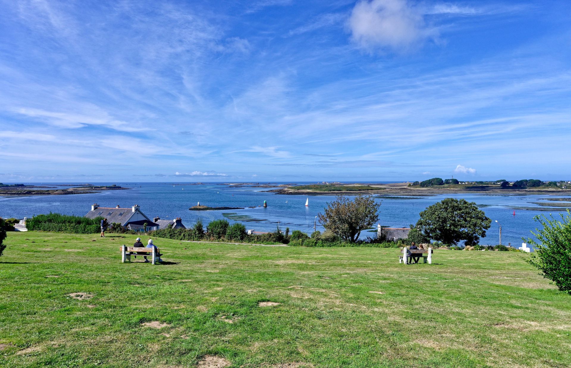 Champ herbeux surplombant une mer calme et bleue et des îles dispersées sous un ciel partiellement nuageux.