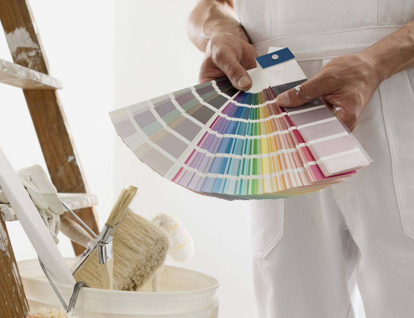 Un peintre en salopette blanche tient un éventail d'échantillons de couleurs et choisit une couleur de peinture ; une échelle et un seau sont visibles.