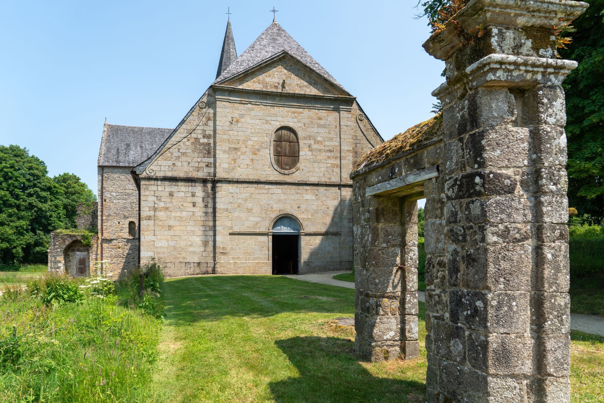 Église en pierre avec porte voûtée et arche en pierre patinée sous un ciel lumineux.
