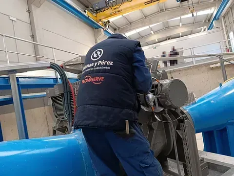 Un hombre con un chaleco azul está trabajando en una máquina en una fábrica.