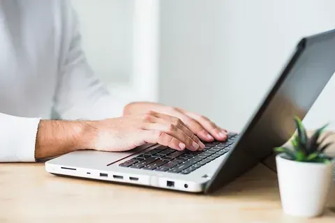 Una persona está escribiendo en una computadora portátil en un escritorio.