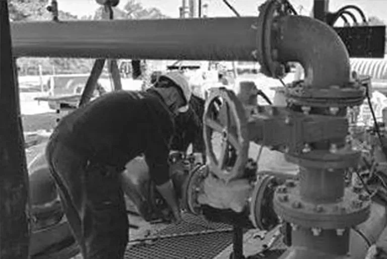 En una fotografía en blanco y negro, un hombre está trabajando en una tubería.