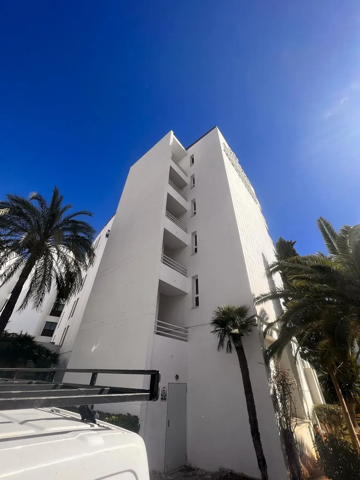 Un edificio alto y blanco con palmeras delante.