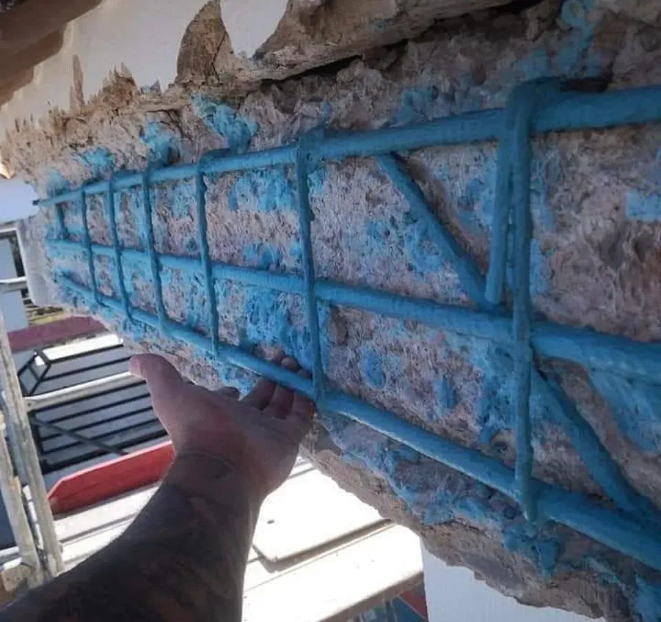 La mano de una persona se introduce en una viga de hormigón con pintura azul.