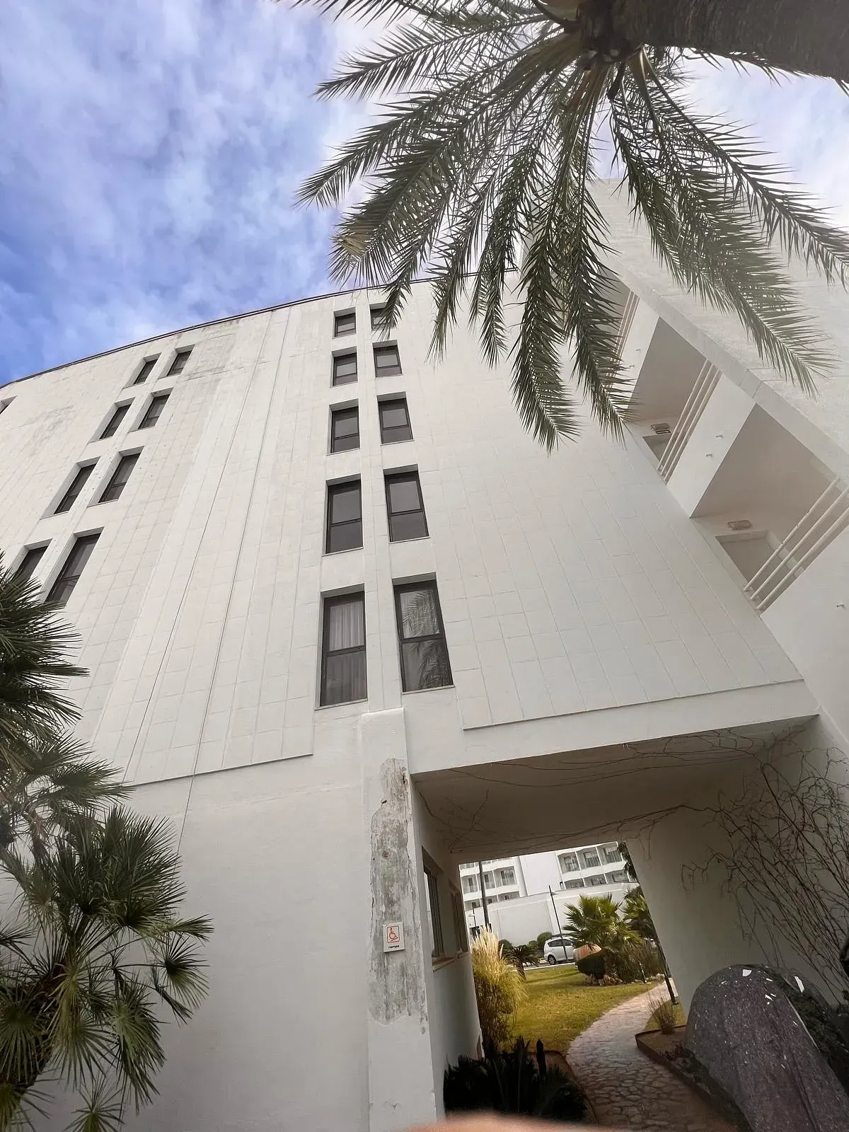 Mirando hacia arriba a un edificio alto y blanco con palmeras frente a él